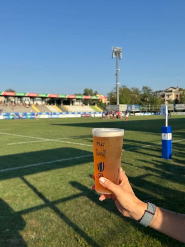 Bicchiere personalizzato FIR pieno di birra, davanti al campo da rugby